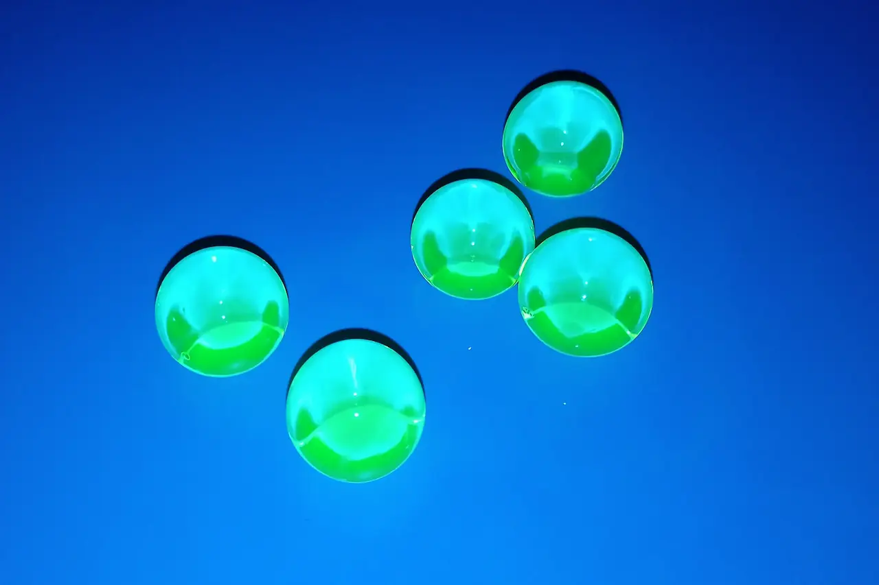 Fotografía de esferas de hidrogel fluorescentes iluminadas con luz ultravioleta.